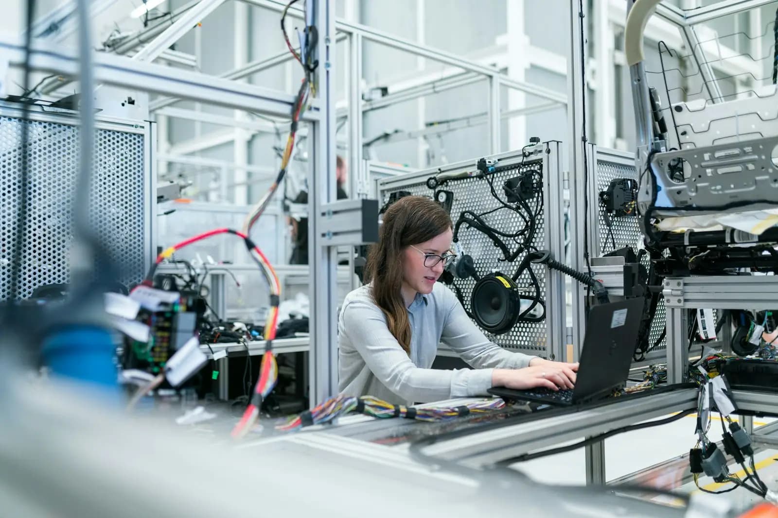 Eine Ingenieurin arbeitet am Laptop in einer automatisierten Fertigungszelle voller Kabel und Sensoren