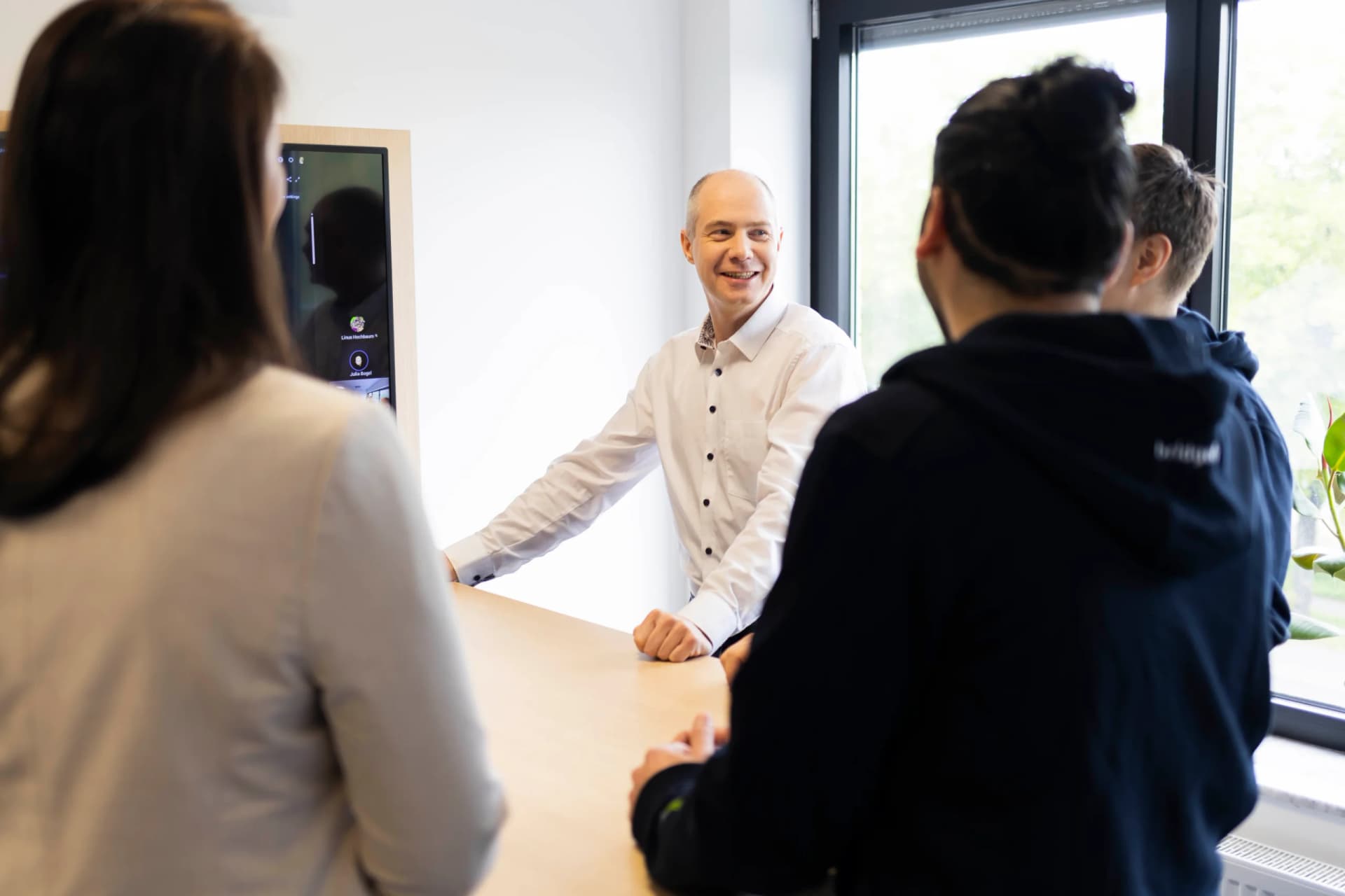 Ein Kollege lacht im Gespräch mit zwei Kolleg:innen am Besprechungstisch
